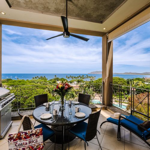 Covered balcony with ocean-view dining table, gas grill, and lounge chair overlooking Tamarindo Bay, Costa Rica.