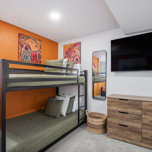 The cheerful fifth bedroom downstairs boasts a stylish dresser, and a large tv, creating a fun and inviting space for relaxation and entertainment!