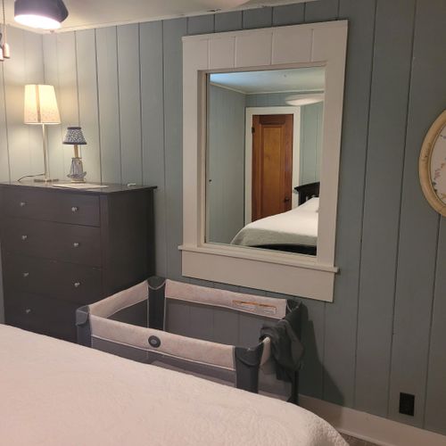 Bedroom #5 (beach house, main floor):  private bedroom with a queen-size bed, ceiling fan, dresser, nightstand, lamp, mirror, and a travel crib.