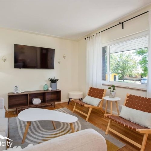 - bright living space with mid century flair, wall mounted tv, and seating for all
- leather woven chairs and a funky coffee table bring fun modern style
- large window fills the room with sunshine and neighborhood views