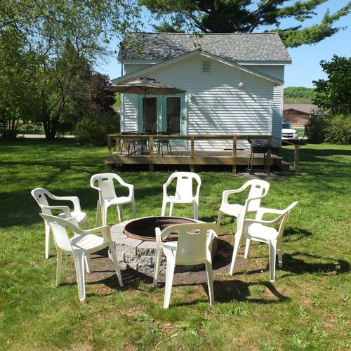 Exterior:  the backyard, which includes a fire ring with chairs, deck, outdoor dining table with chairs, and a charcoal grill.
