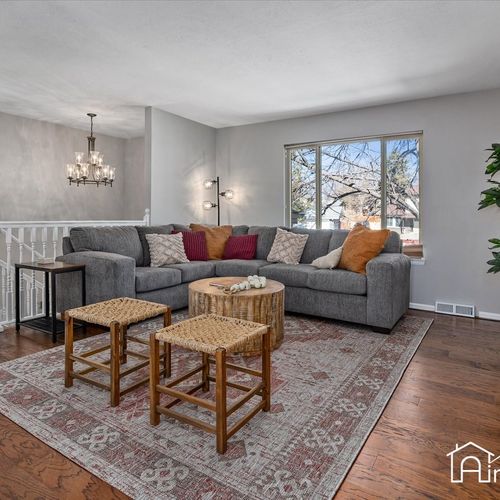 - spacious living area with a large gray sectional and layered rugs for cozy lounging
- wood coffee tables and woven stools bring a rustic charm to the modern setting
- natural light fills the space through wide windows and warm toned hardwood floors