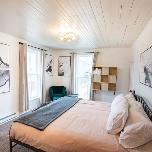 - stylish room featuring bold framed artwork, a plush velvet chair, and soft toned bedding
- floor to ceiling windows fill the space with light and wintery outdoor scenery
- functional storage, neutral palette, and statement lighting complete the ele