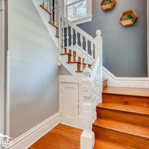 - historic charm shines through the white painted banister and classic wood steps
- honeycomb wall planters and natural window light create a welcoming entryway
- unique under stair storage door adds character and functional design