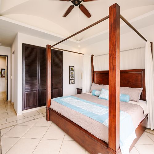Master bedroom with tropical hardwood four-poster canopy king bed, tray ceiling fan, and sliding door to Tamarindo ocean view.