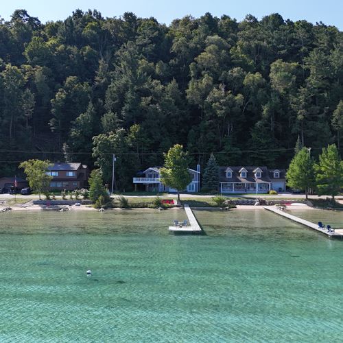 OVERVIEW:  Aerial view from over Crystal Lake of the cottage, dock, and bonfire ring, with the mooring buoy for the property also shown in the photo.