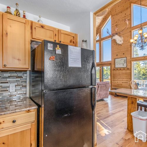 - black fridge and wood cabinets blend beautifully in this mountain style kitchen design
- steps away, the dining area glows with natural light and soaring wood paneled ceilings
- perfect setup for family dinners or laid back brunches with a view