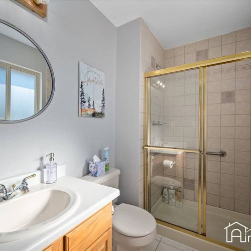 - full bathroom with gold framed glass shower, tile walls, and light wood vanity cabinet
- round mirror and wall art add charm while offering all the essentials you need
- clean and functional setup perfect for refreshing morning routines