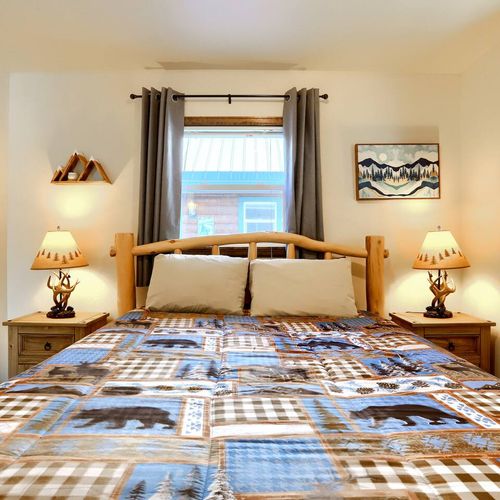 - cabin comfort shines in this bedroom with dual nightstands, carved lamps, and a patchwork bear quilt
- center window brings in cheerful daylight with blackout curtains for privacy
- woodsy details and a mountain art piece add tranquil lodge flair
