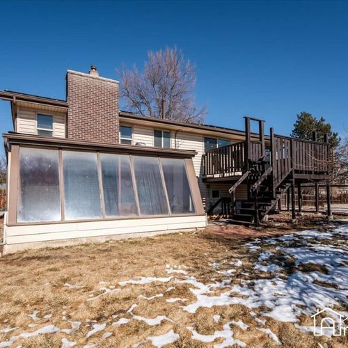 - rear view of home showcasing the enclosed sunroom and upper level back deck
- wood staircase leads to spacious outdoor living areas perfect for entertaining
- bright and open yard provides room to relax, roam, or gather year round