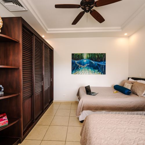 Guest bedroom interior showing louvered wood closets, shelves with coral decor, and board games including Monopoly.