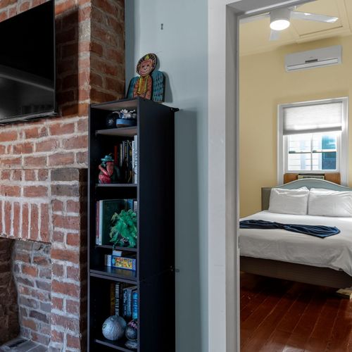 Sunlit bedroom corner w/ exposed brick & cozy, lived-in warmth.