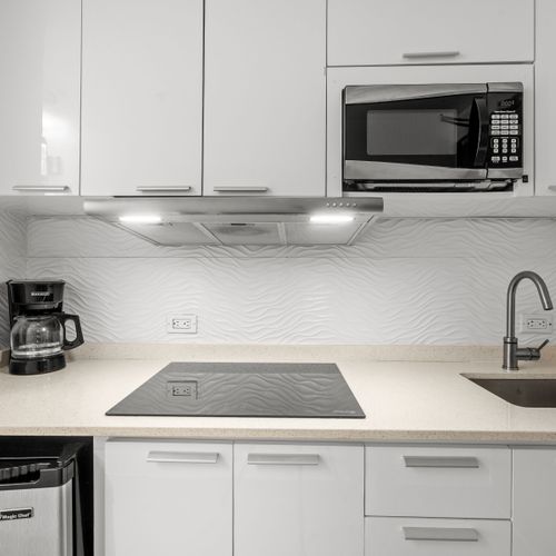 Whip up delicious meals in your fully equipped, modern kitchen featuring sleek white cabinetry, a microwave, and a convenient cooktop. Perfect for preparing your morning coffee or a gourmet dinner!