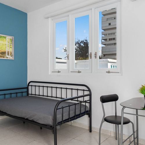 Modern room with cozy sofa bed with soft texture and clean modern kitchennette, airconditioner, window with natural light, white walls, cozy lights