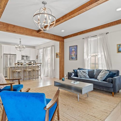 Open-concept living & dining area w/ chandelier & bold blue statement pieces.