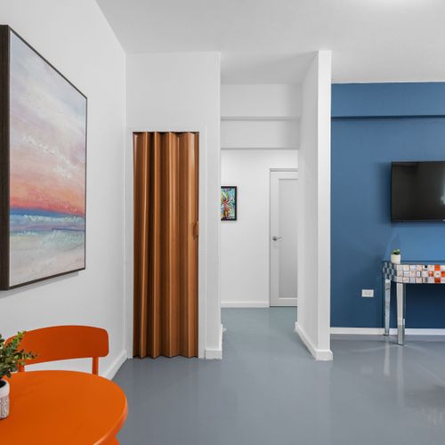 A modern, colorful room with a blue accent wall, white rocking chairs, and a flat-screen TV, showcasing a world map and abstract art on the walls, creating a lively and comfortable space.