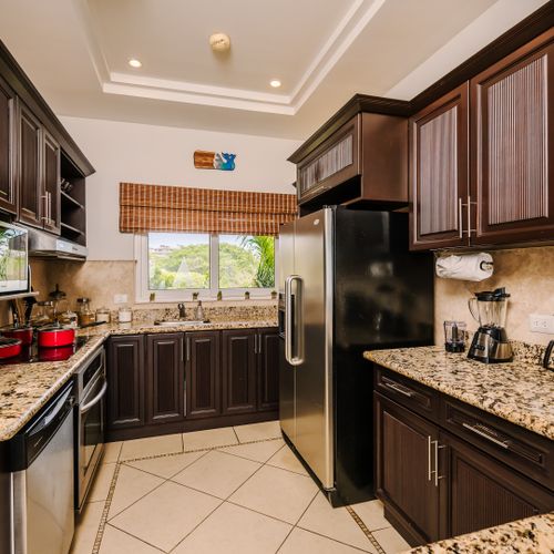 Kitchen at dusk with recessed tray-ceiling cove lighting, dark cabinetry silhouetted, and warm accent light over the arched sculpture niche.