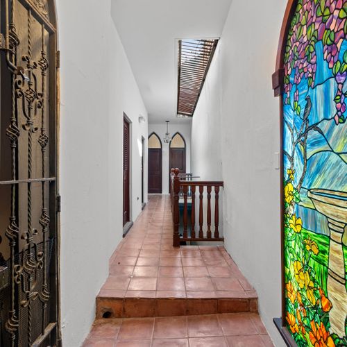 This hallway is the entrance to our home and is filled with natural light and beautiful stained glass windows. The hallway is tiled with terracotta tiles and has a wooden railing.
