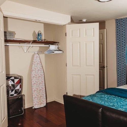 Open closet with storage space, an ironing board, and essentials.