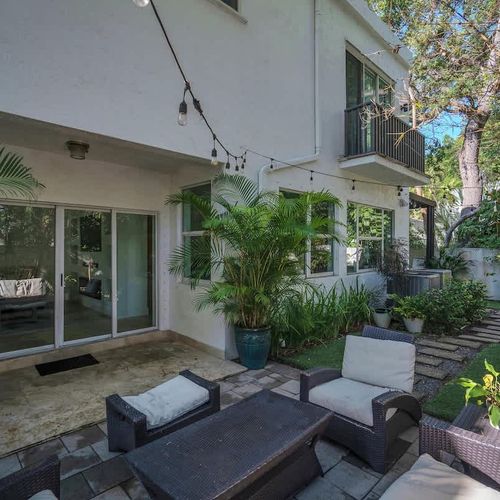 Relax in a lush backyard retreat with cozy seating, tropical plants, and string lights—perfect for unwinding day or night.