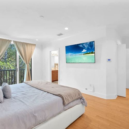 Spacious bedroom retreat with a plush bed, balcony access, and a sleek TV. Enjoy natural light, fresh air, and a relaxing ambiance.