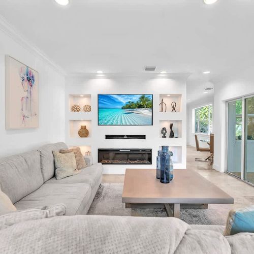Relax in this bright, stylish living room featuring a plush sectional, large TV, and modern décor. Enjoy a movie, read a book, or soak in the seamless indoor-outdoor flow—perfect for unwinding.