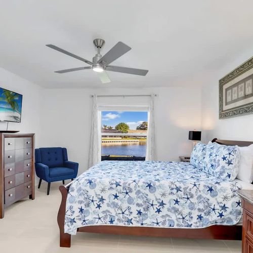 Bedroom 1 features a spacious queen bed with plush pillows, crisp linens, a private TV, and tranquil lake views right outside the window.