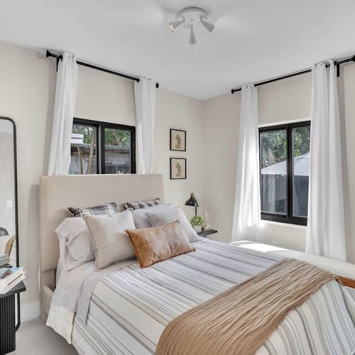 Bright and inviting bedroom featuring soft neutral tones, cozy layered bedding, and natural light streaming.