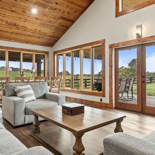 Relax in this warm, inviting space featuring a spacious living, dining, and kitchen area with glass doors and windows framing the relaxing countryside scenery.