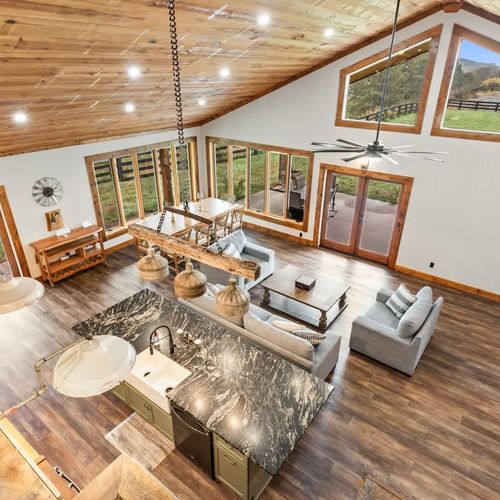 Relax in this warm, inviting space featuring a spacious living, dining, and kitchen area with glass doors and windows framing the relaxing countryside scenery.
