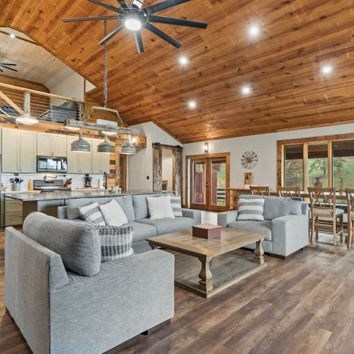 Relax in this warm, inviting space featuring a spacious living, dining, and kitchen area with glass doors and windows framing the relaxing countryside scenery.