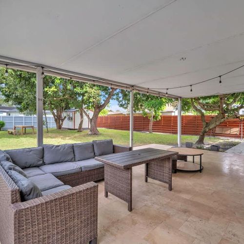 Relax in a spacious, fully fenced backyard with lush green space, shady trees, a charming swing set, and a patio perfect for outdoor lounging.