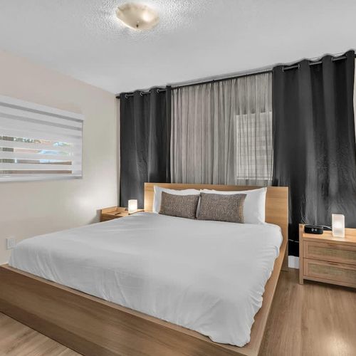 Relax in a clean, modern bedroom with cozy bedding, warm wood accents, and plenty of natural light.