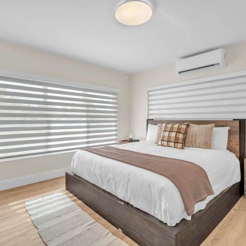 Relax in a clean, modern bedroom with cozy bedding, warm wood accents, and plenty of natural light.