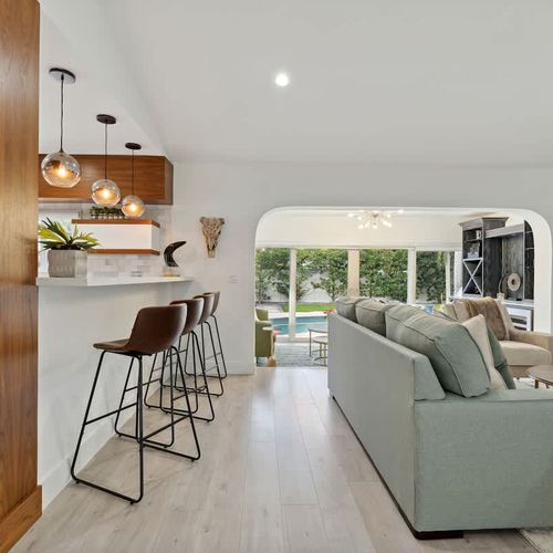 Spacious main living room with a queen-size sofa bed, modern seating, and open-concept design flowing into the kitchen and pool-view areas.