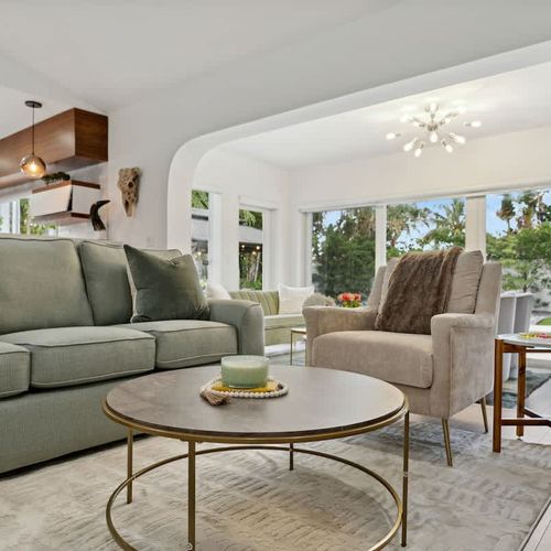 Spacious main living room with a queen-size sofa bed, modern seating, and open-concept design flowing into the kitchen and pool-view areas.