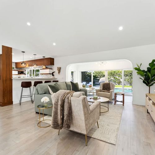 Spacious main living room with a queen-size sofa bed, modern seating, and open-concept design flowing into the kitchen and pool-view areas.