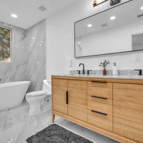 Spacious and functional bathroom with a bathtub, large mirror, and dual sinks.