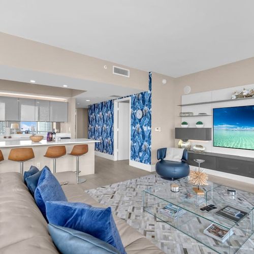 Spacious living area featuring a large flat-screen TV and a modern kitchen with a breakfast counter and stylish bar seating.