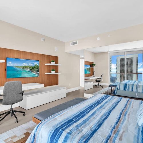 Modern, sunlit bedroom with a king-size bed, workspace, and private balcony offering beautiful ocean and city views. ️