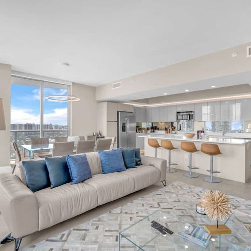 Spacious living area featuring a large flat-screen TV and a modern kitchen with a breakfast counter and stylish bar seating.