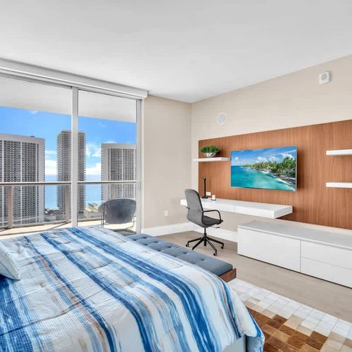 Modern, sunlit bedroom with a king-size bed, workspace, and private balcony offering beautiful ocean and city views. ️