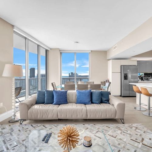 Spacious open-concept living space featuring a cozy sofa, dining area, and expansive windows showcasing stunning ocean and city views.