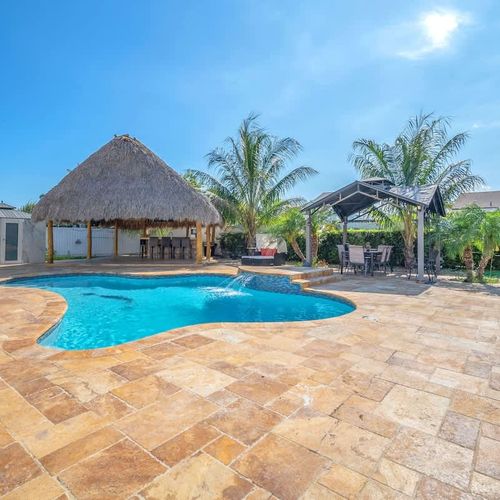 Resort-style pool with tropical tiki hut and lush palm surroundings.