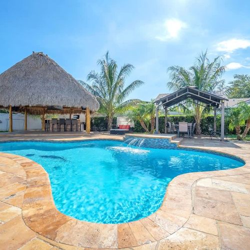 Sparkling pool with waterfall feature, surrounded by a sunny patio and shaded lounge areas.