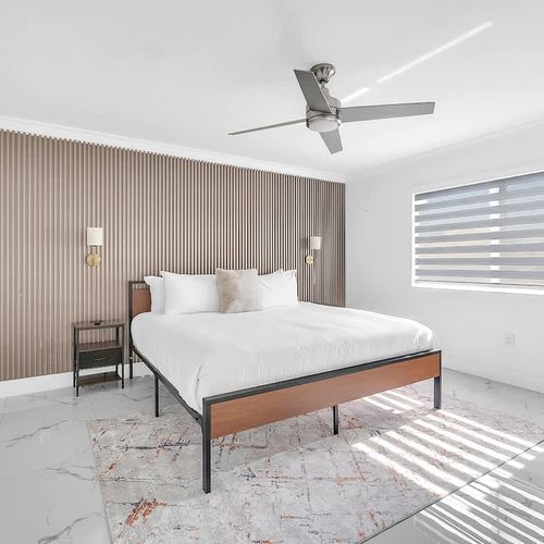 Bright, modern primary bedroom with a king bed, stylish wood accent wall, and plenty of natural light.