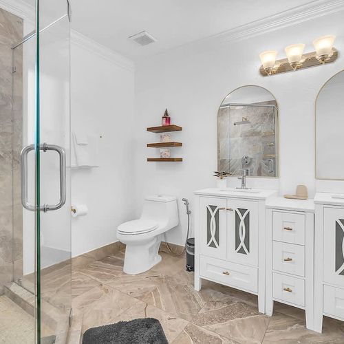 Beautifully designed bathroom with dual sinks, arched mirrors, and a spacious glass-enclosed shower—perfect for getting ready with ease.