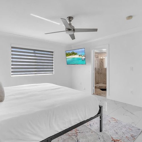 Bright and spacious bedroom featuring a comfortable bed, smart TV, and direct access to a private bathroom and walk-in closet.