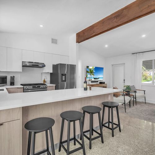 Fully equipped modern kitchen featuring sleek white cabinetry, stainless steel appliances, and a spacious island with bar seating