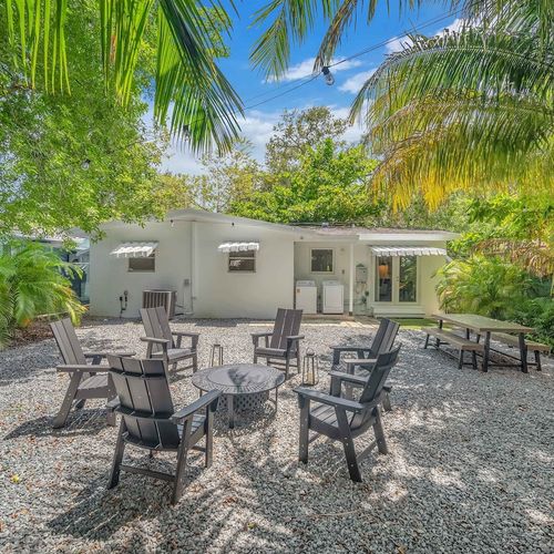Private backyard retreat featuring a firepit with seating, picnic-style dining table, and a grill for al fresco cooking under the palms.